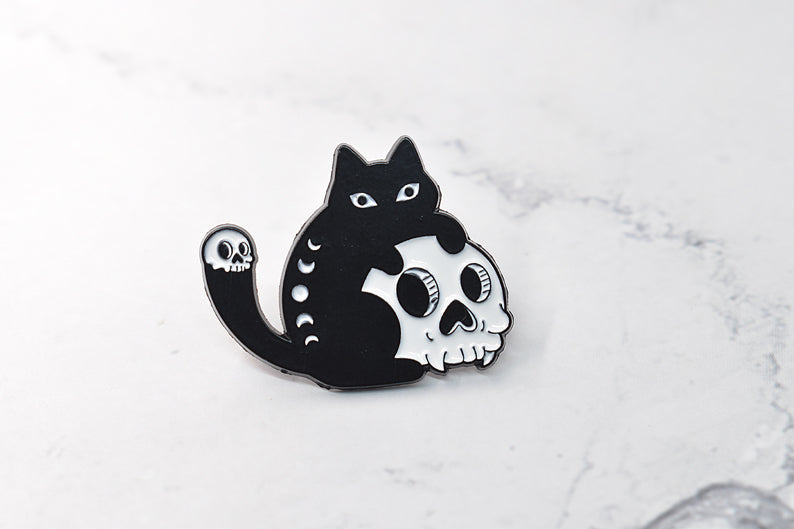 Enamel pin with black cat holding a skull